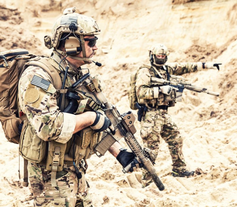 Two armed US army commandos or military scouts equipped with radio headset moving forward in sands during enemy area reconnaissance. Special forces operation, long range surveillance mission in desert